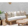 rattan sofa with white seat cushions sitting against a white wall