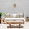rattan sofa with white seat cushions sitting against a white wall