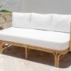 rattan sofa with white seat cushions sitting against a white wall
